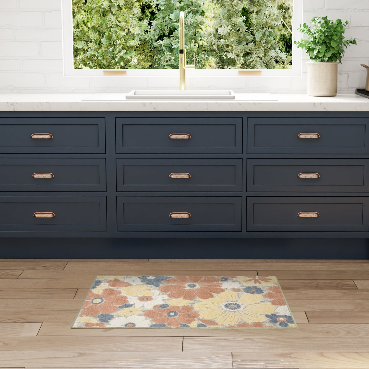 Navy blue nine-drawer kitchen cabinets with brass pulls, white countertop, gold faucet, and colorful floral rug on wood floor.