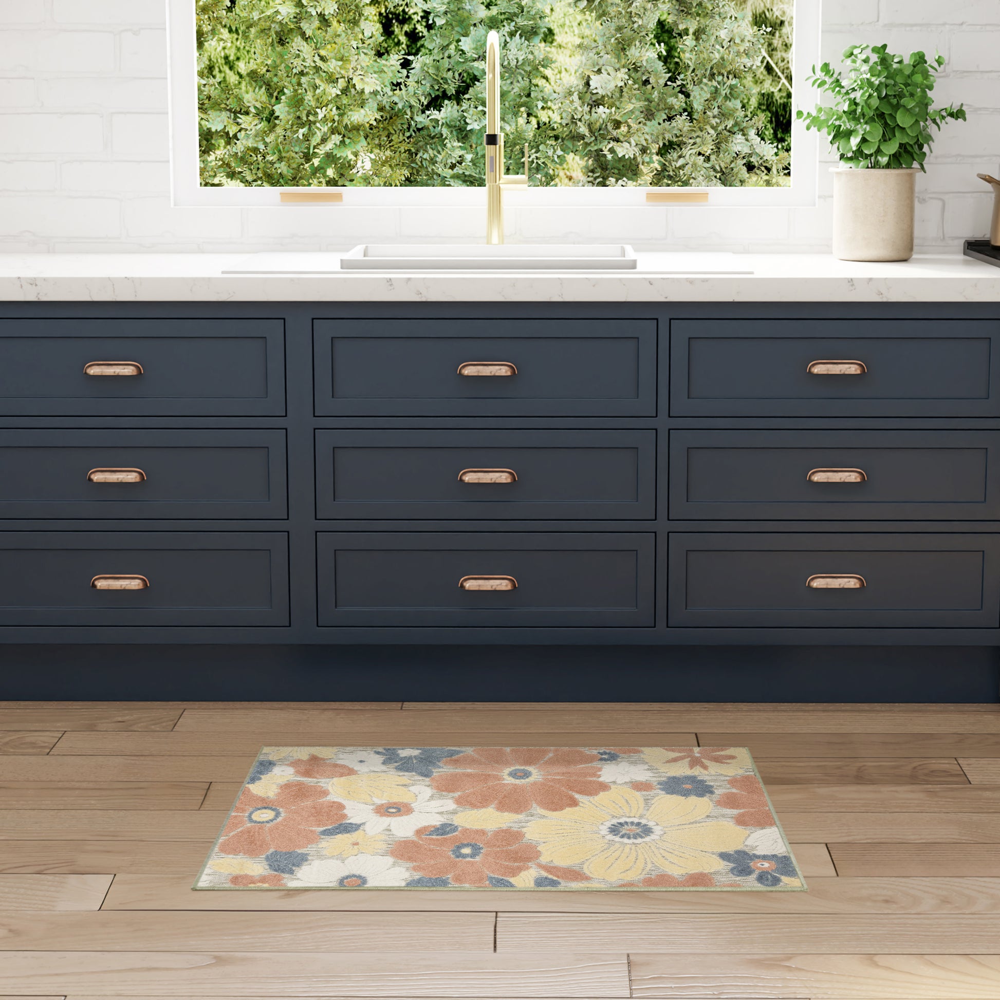 Navy blue nine-drawer kitchen cabinets with brass pulls, white countertop, gold faucet, and colorful floral rug on wood floor.