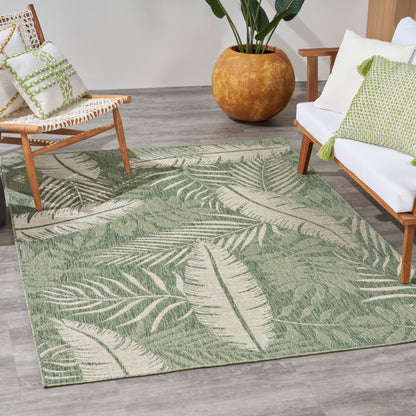 Green tropical leaf rug on gray wood floor, framed by wooden chairs with white cushions and a large terracotta pot.