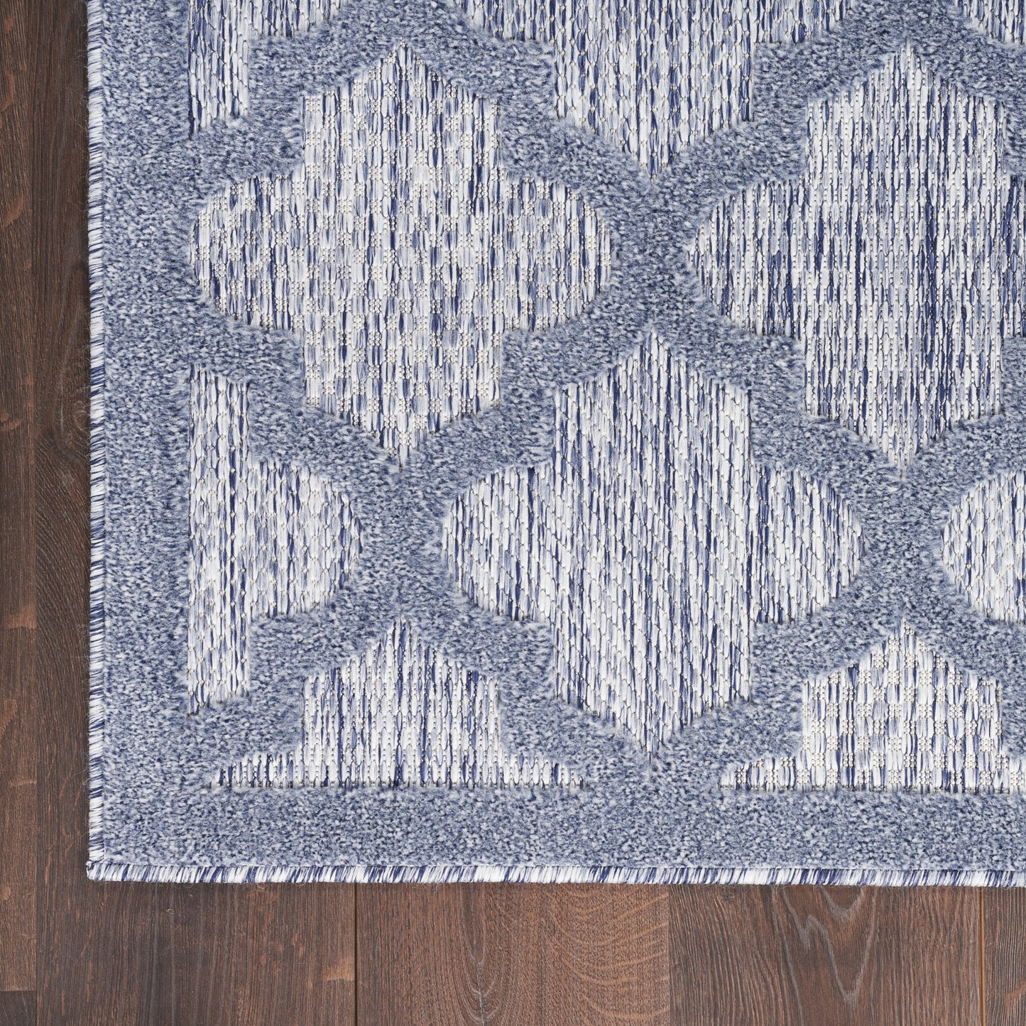 Blue and white geometric area rug with diamond lattice pattern on dark wood floor.