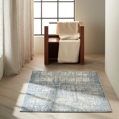 Cream throw on dark wood armchair by grid window, beige curtains, blue abstract rug on light wood floor.
