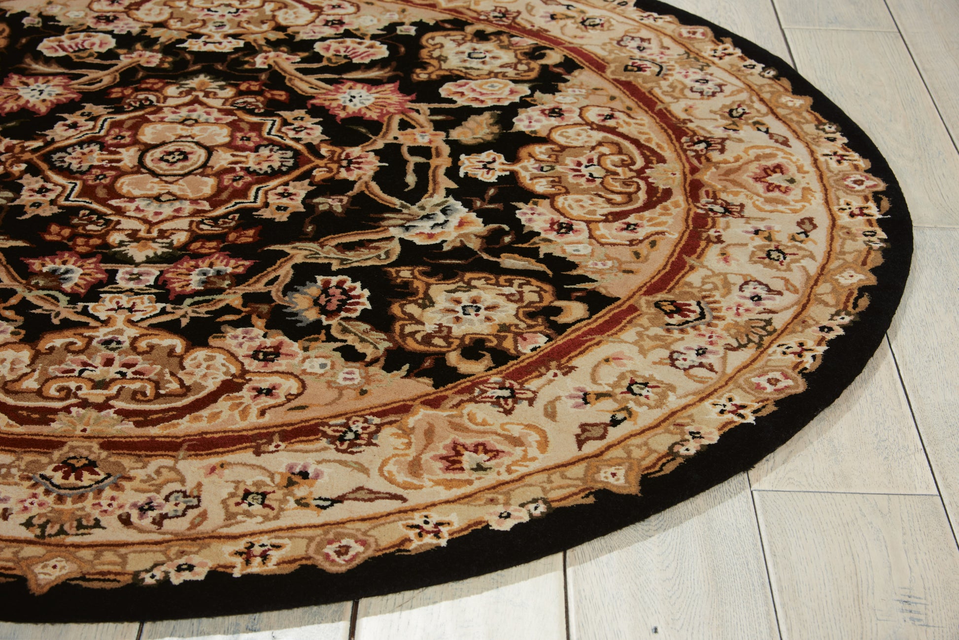 Round oriental rug with black central field, ivory and red border, floral motifs, on light wood floor.