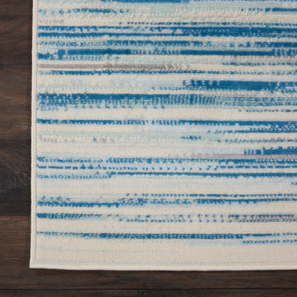 Blue and white striped area rug with brushstroke bands and a cream border, resting on dark wooden floor.