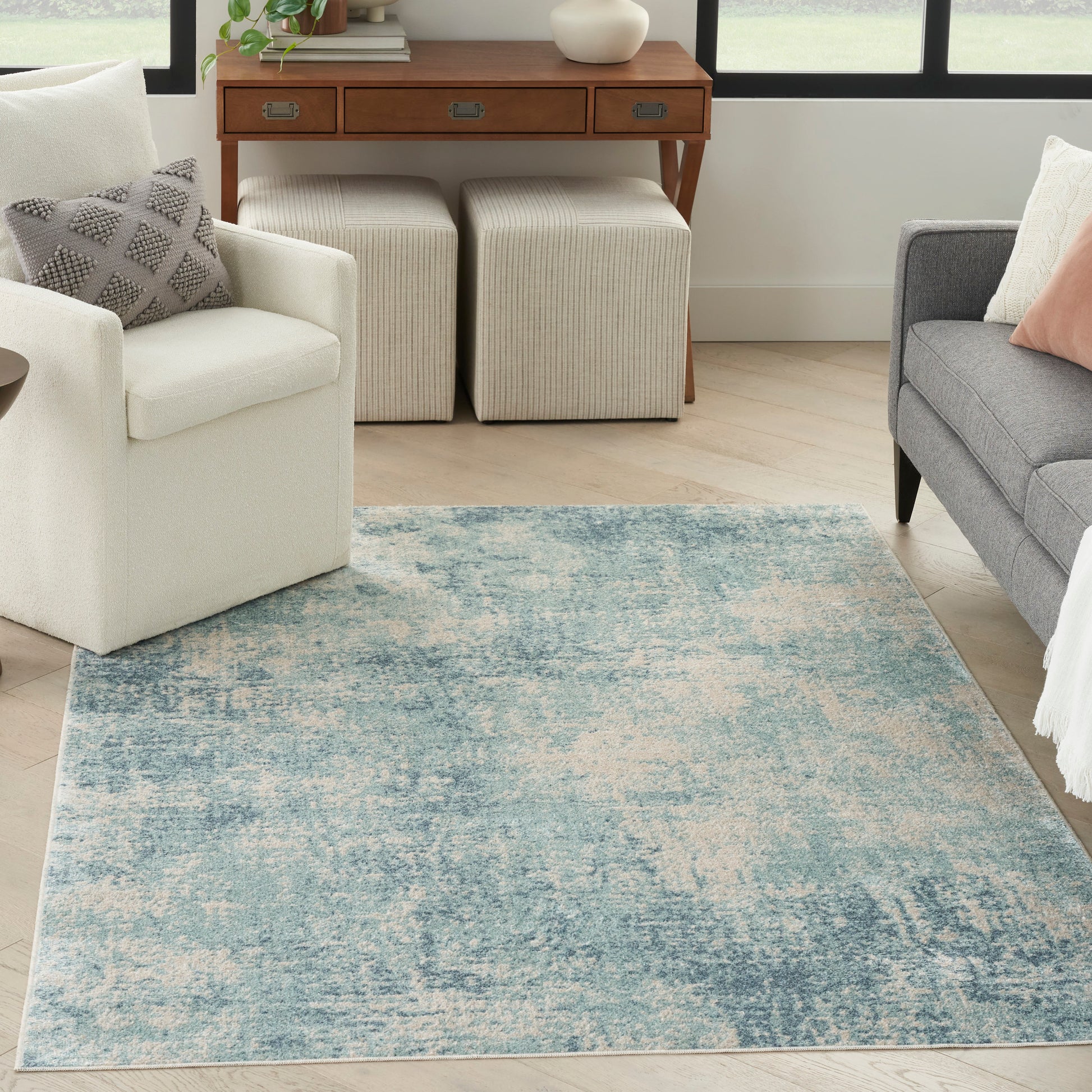 Soft blue distressed area rug on light hardwood, with white armchair, gray sofa, beige ottomans and wooden console.