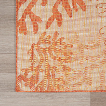 Rectangular woven rug with orange botanical motif on beige background and orange border, placed on a wooden floor.