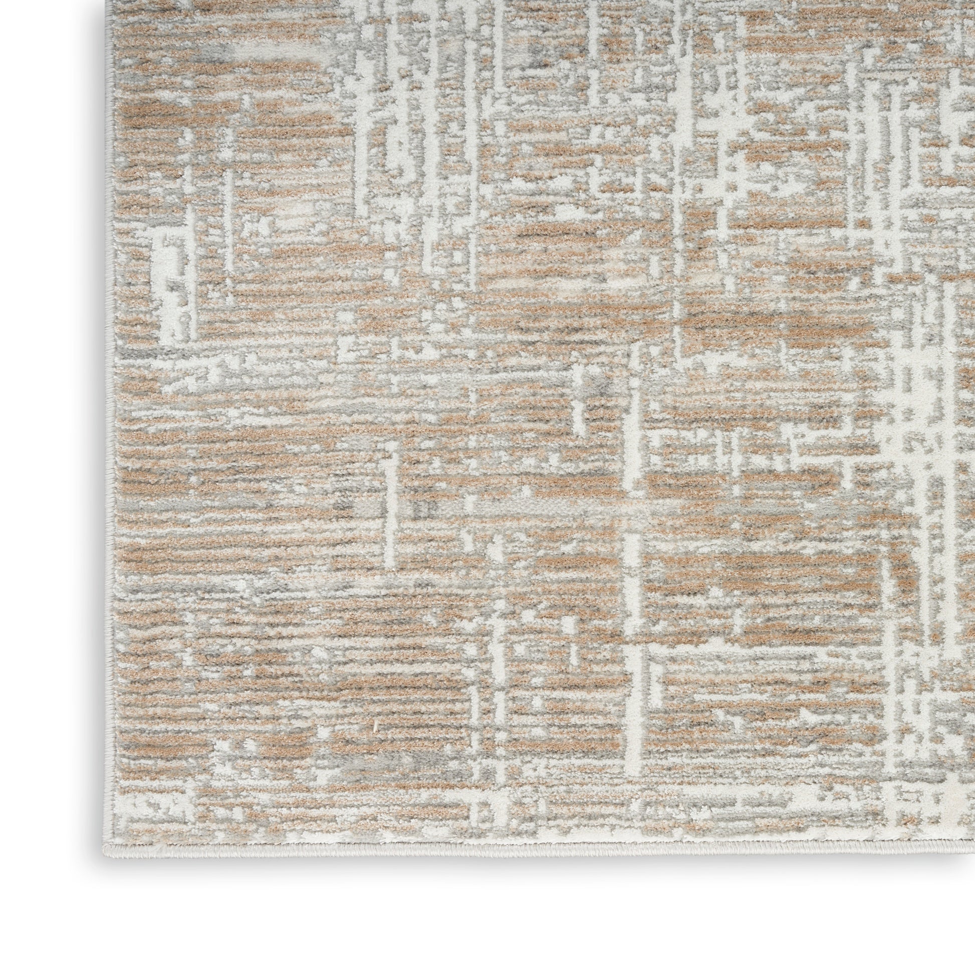 Rectangular beige and taupe area rug with white abstract geometric pattern and plush textured pile.