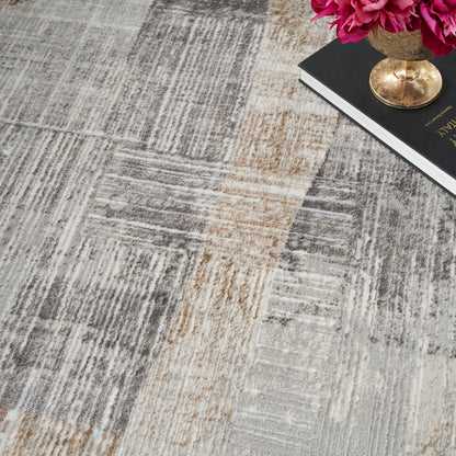 Modern patchwork area rug in gray and beige tones; low-pile woven texture, shown with pink flowers and a gold vase.