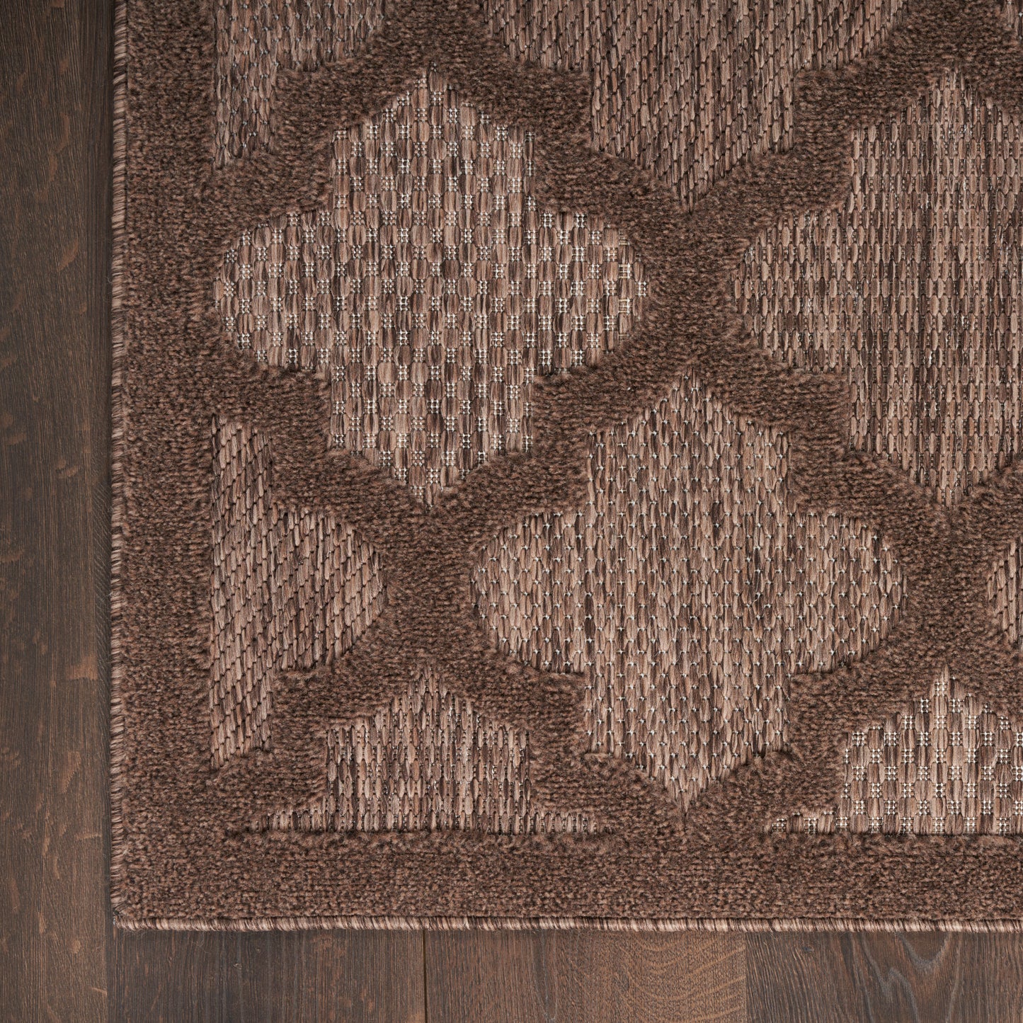 Brown geometric rug with large light-beige quatrefoil pattern, textured shag pile, dark border on wood floor.
