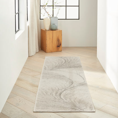 Long light gray rug runner with subtle circular wave pattern on pale wood floor in bright hallway by a window.