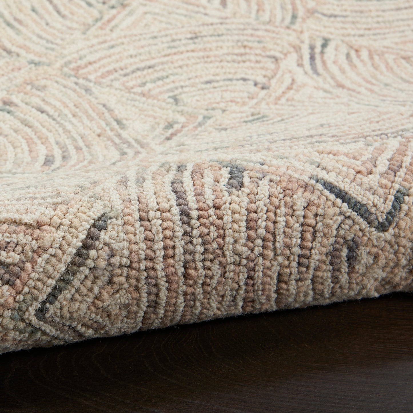 Beige tufted rug with cream and taupe geometric pattern, looped pile, edge folded on dark wood floor.