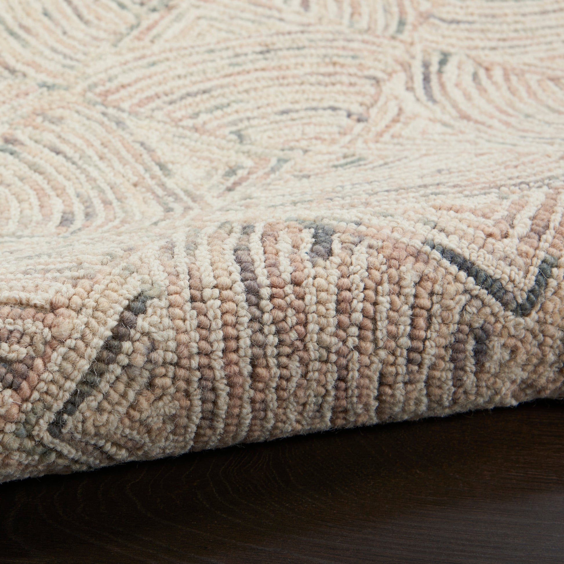 Beige tufted rug with cream and taupe geometric pattern, looped pile, edge folded on dark wood floor.