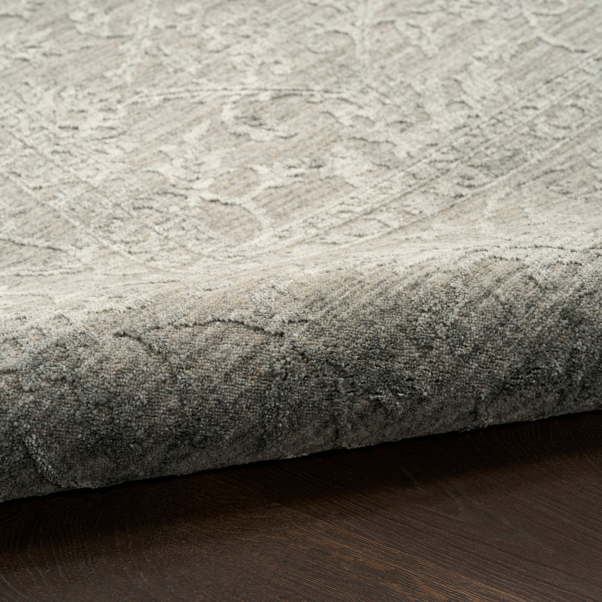 Close-up of a light gray, textured rug with a rolled edge on a dark wood floor.
