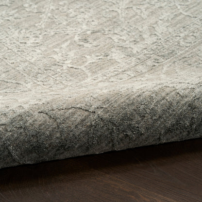 Close-up of a light gray, textured rug with a rolled edge on a dark wood floor.