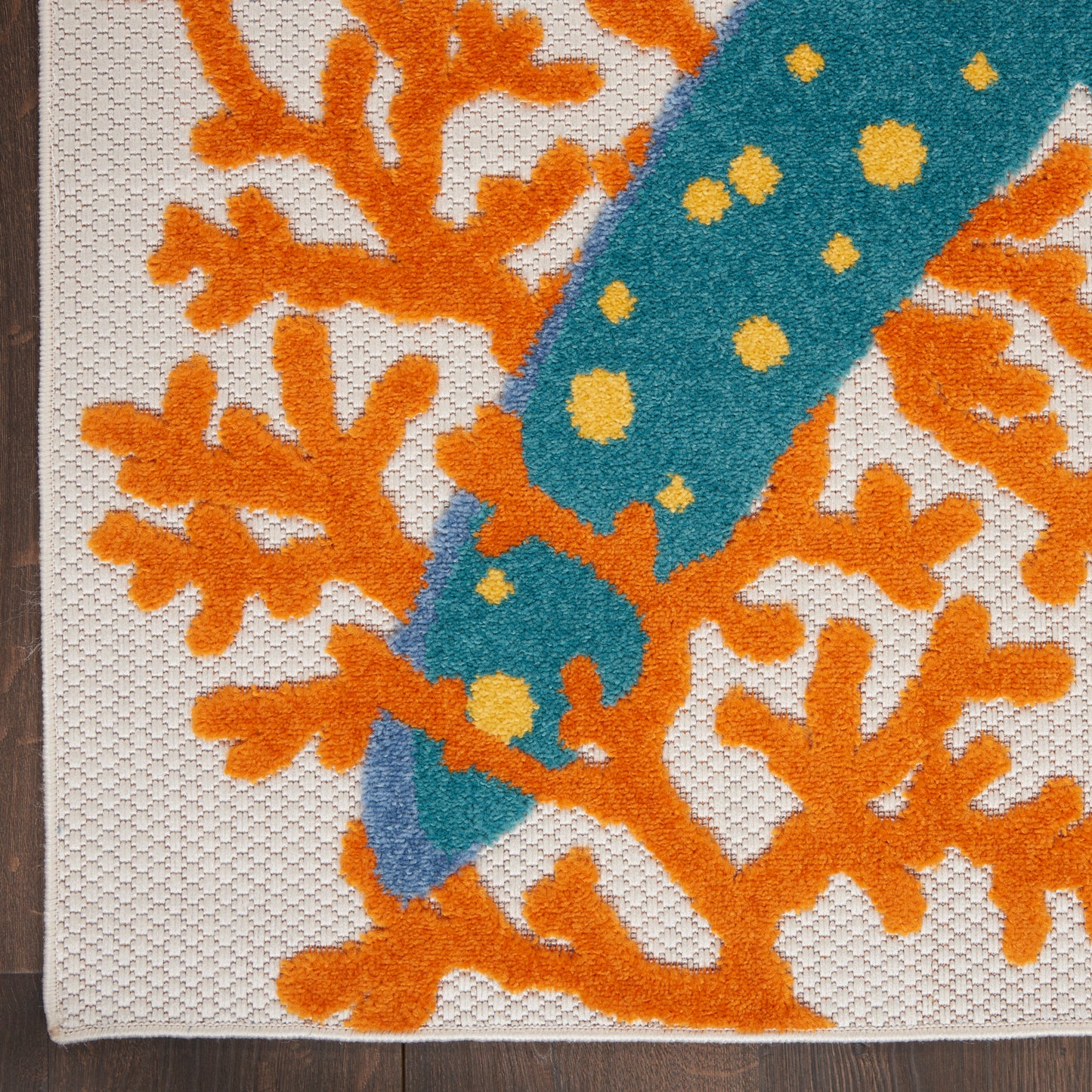 Close-up of orange coral-patterned textile with a teal diagonal dotted band across white canvas.