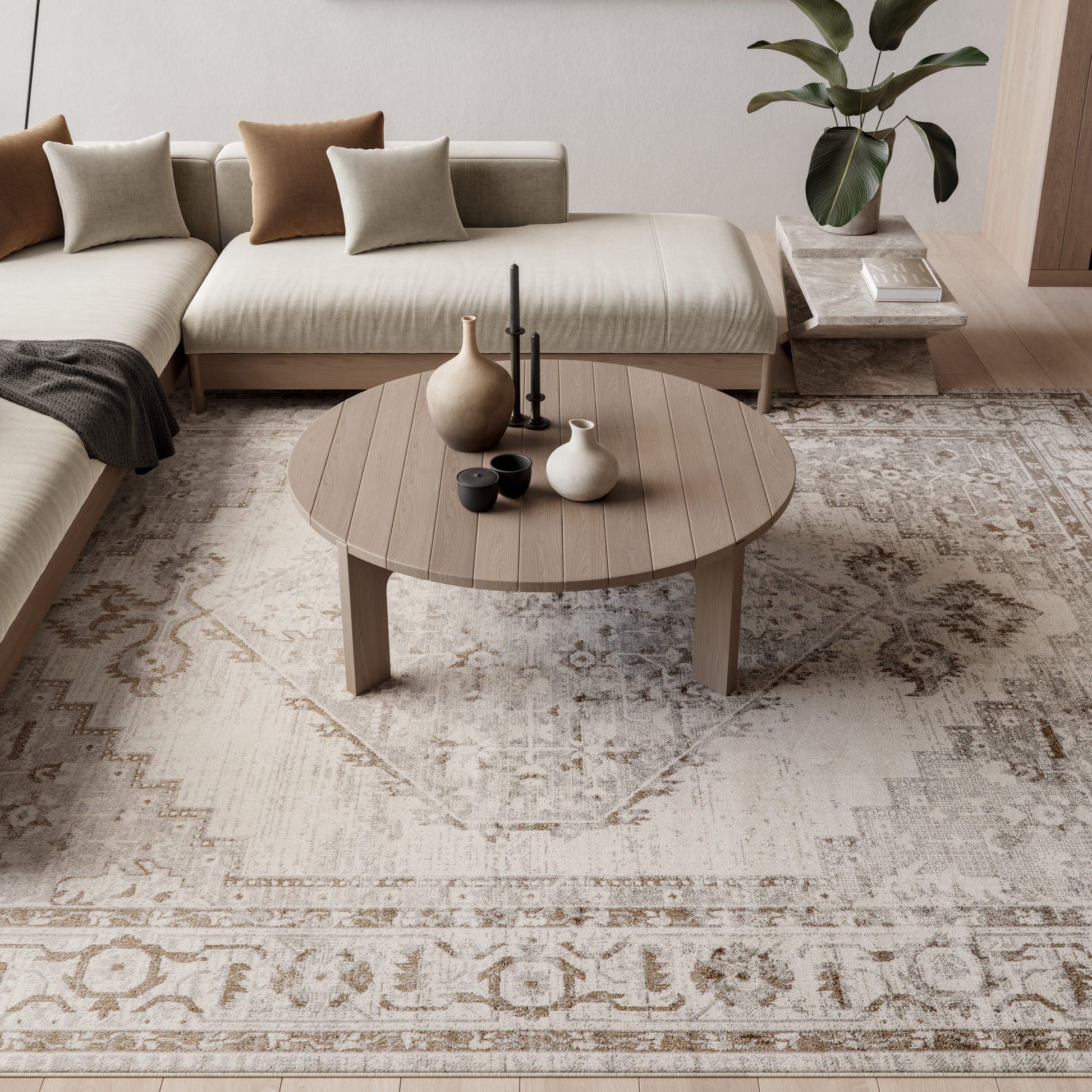 Vintage 8' x 10' beige patterned area rug in a neutral living room with a sectional; round wooden coffee table with vases and candles resting on the rug.