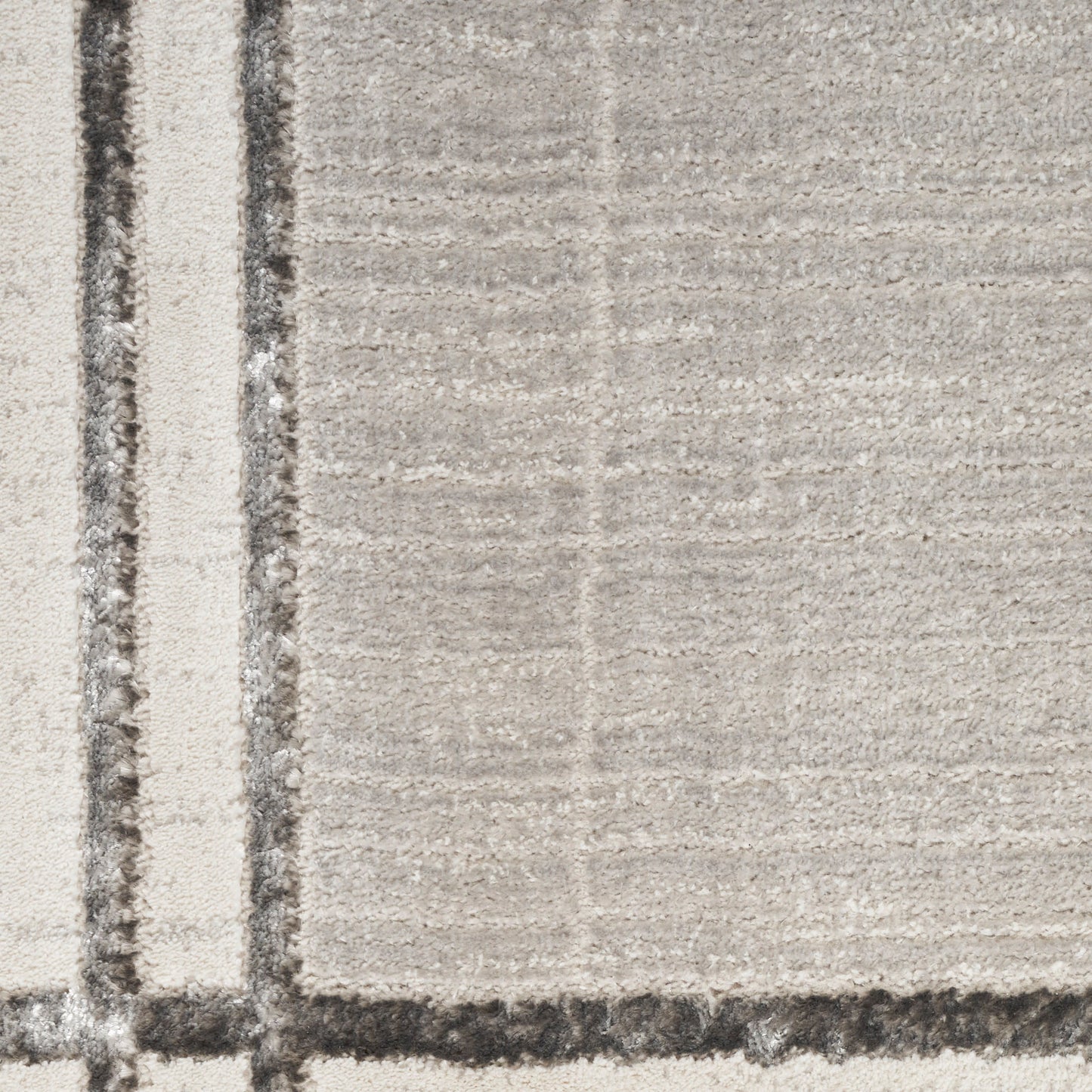 Beige rug with subtle grid pattern and a bold vertical border stripe along the left edge; modern textured look.