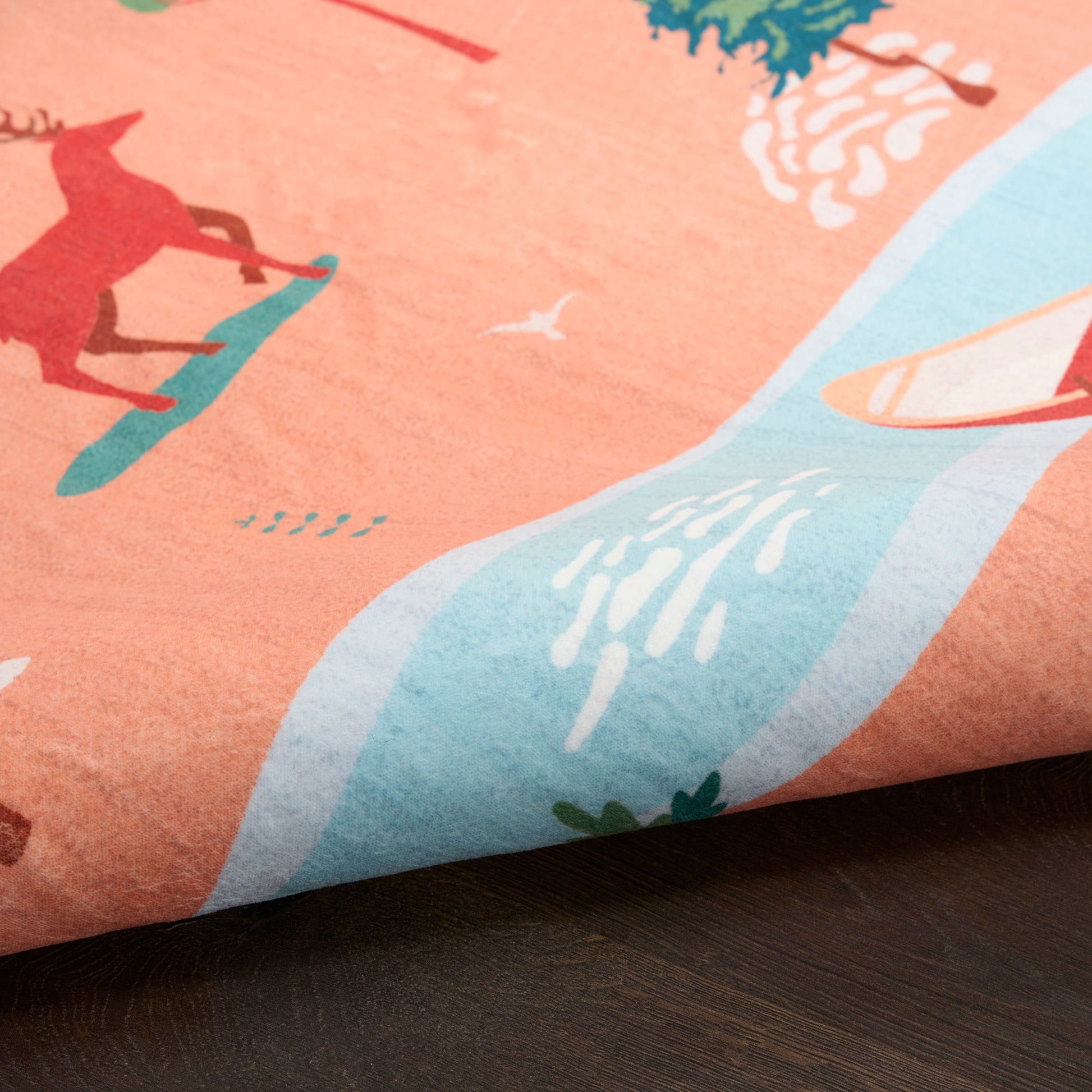 Coral pink rug with a beach print: red figure on a teal board, pale blue wave, white seabird accents.