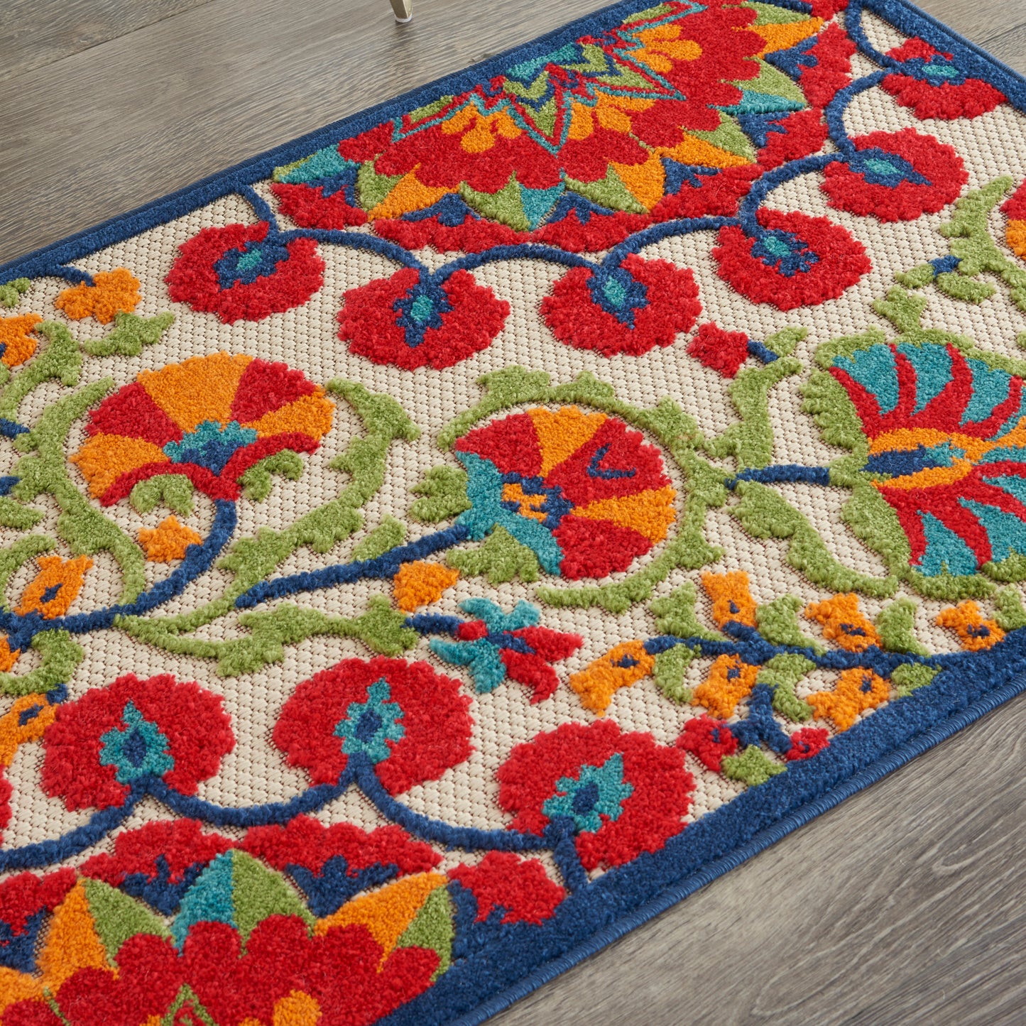 Colorful floral area rug with red, orange, teal and lime green motifs on a cream background; blue border on a wooden floor.