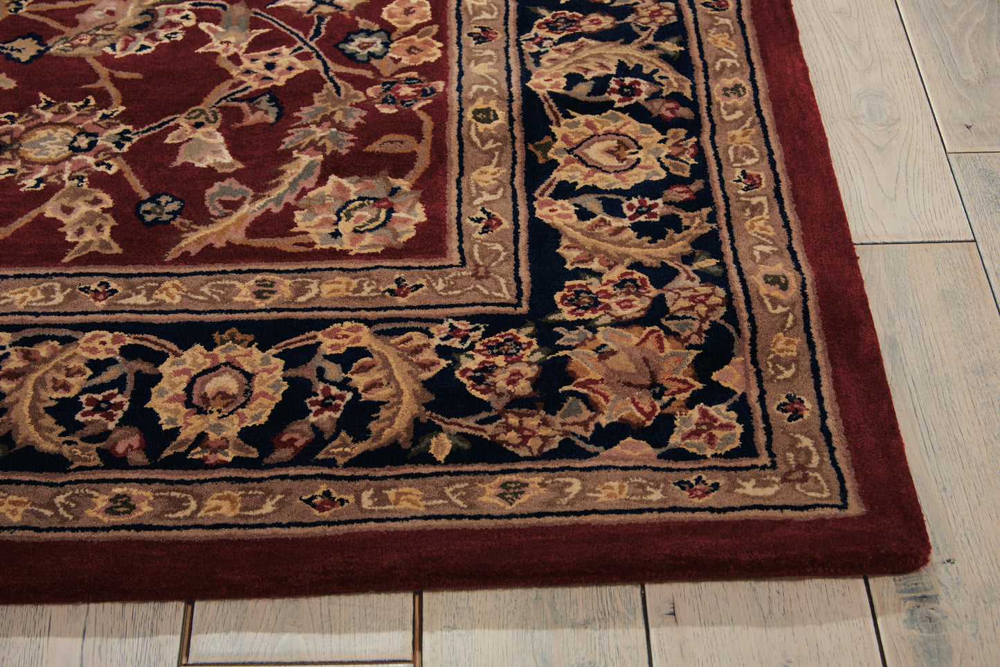 Rectangular oriental rug with burgundy field, intricate beige-gold border and floral motifs on a light wood floor.