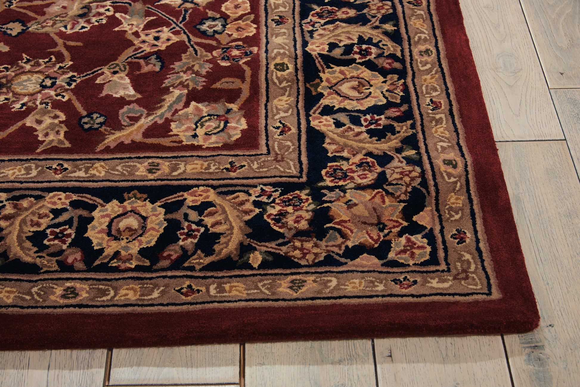 Rectangular oriental rug with burgundy field, intricate beige-gold border and floral motifs on a light wood floor.