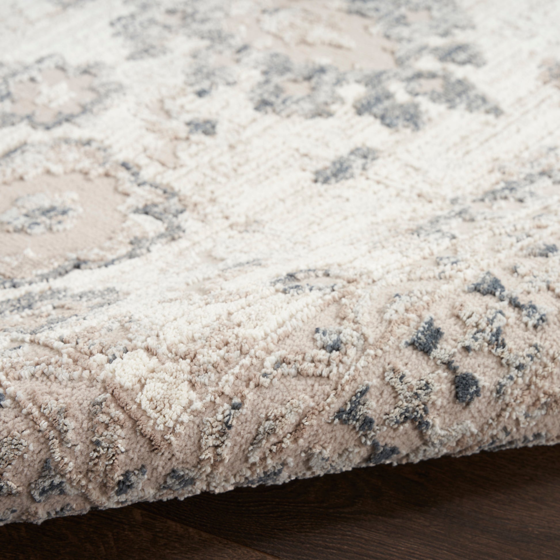 Beige oriental rug close-up, cream and taupe floral pattern with gray accents, soft plush pile on dark wood floor.