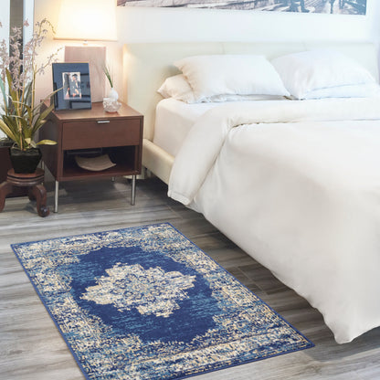 Rectangular blue distressed rug with cream medallion pattern on gray wood floor beside white bed and dark wood nightstand.