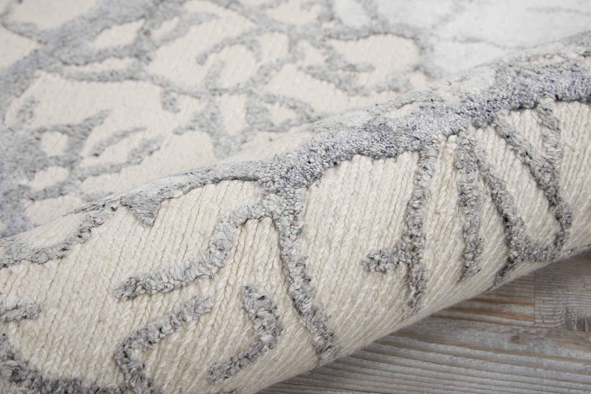 Cream rug with soft gray raised geometric pattern, plush pile, rolled edge on wooden floor.
