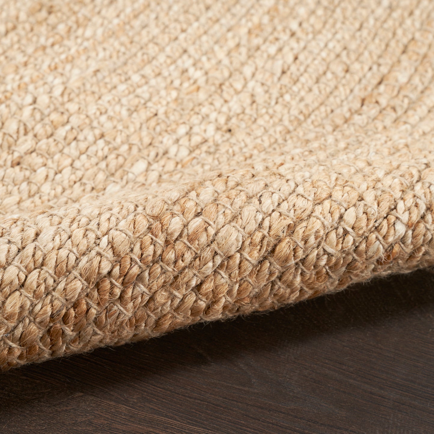 Natural beige jute braided rug close-up with a folded edge on dark wood floor.