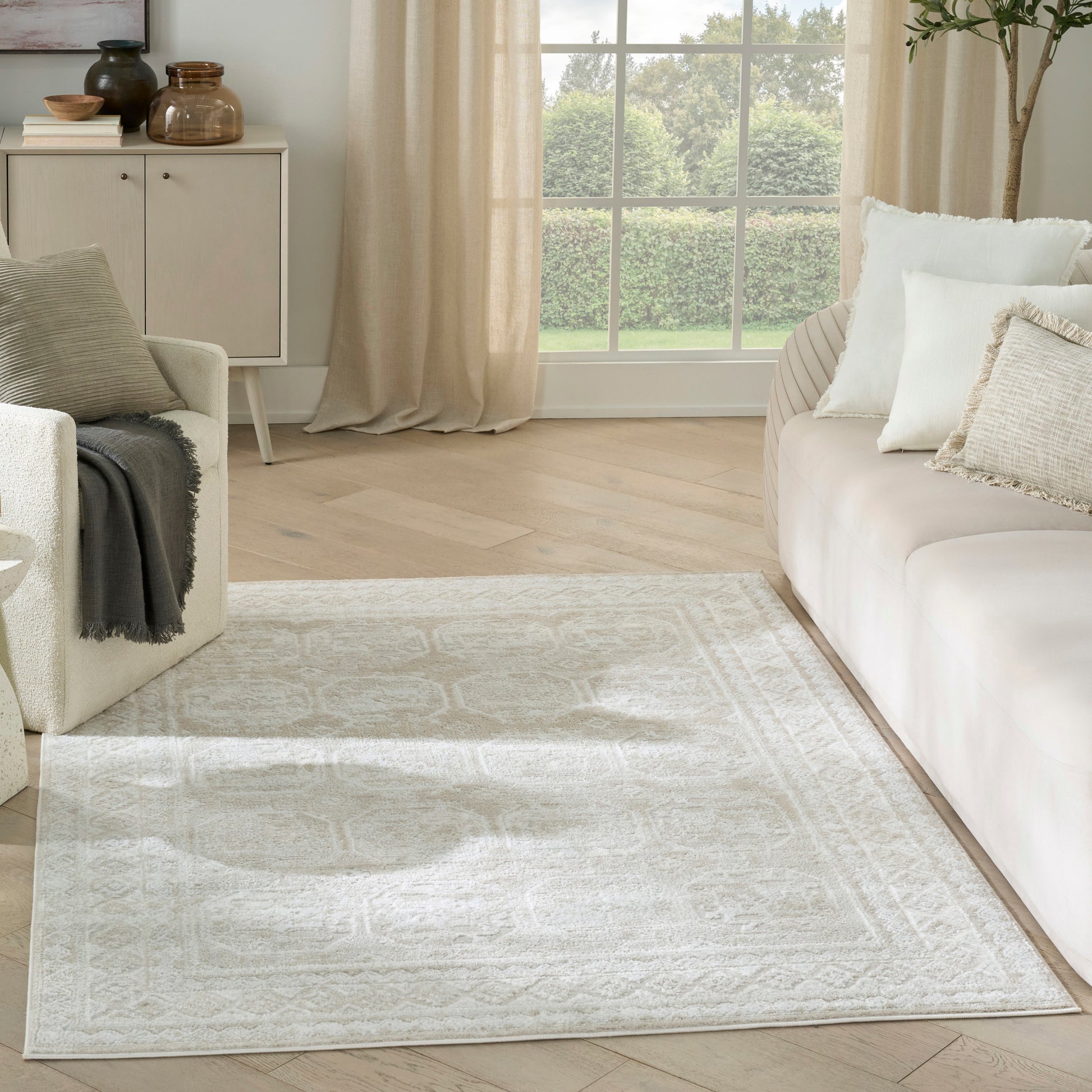 Cream area rug with subtle geometric pattern, laid on light wood floor in neutral living room with beige sofa.
