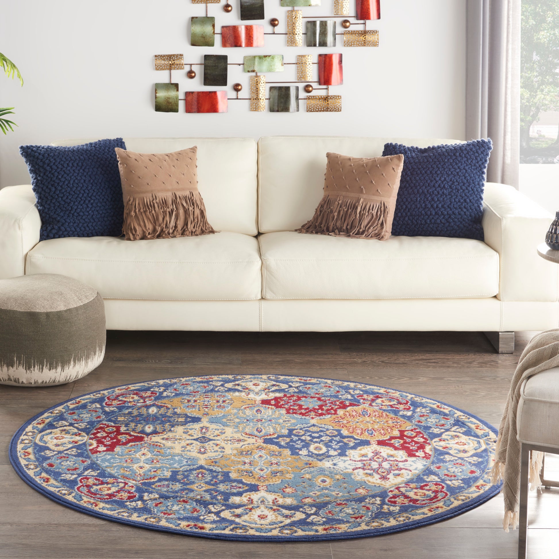 Round oriental area rug with blue, red and beige pattern in front of a cream sofa with navy and tan cushions.