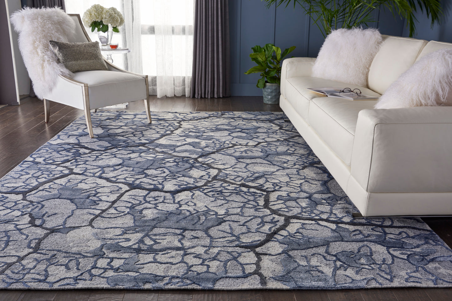 Blue & gray cracked-pattern area rug in a living room with white sofa & armchair, fluffy cushions.