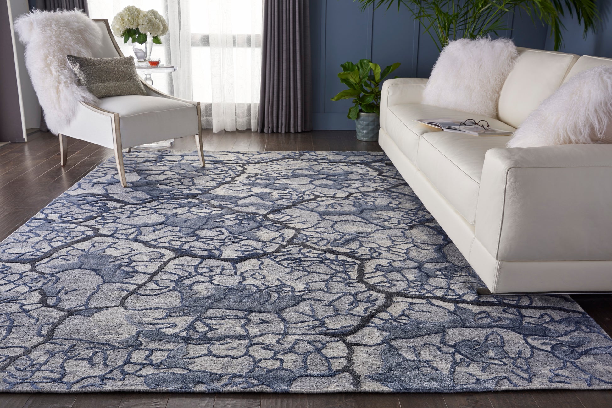 Blue & gray cracked-pattern area rug in a living room with white sofa & armchair, fluffy cushions.