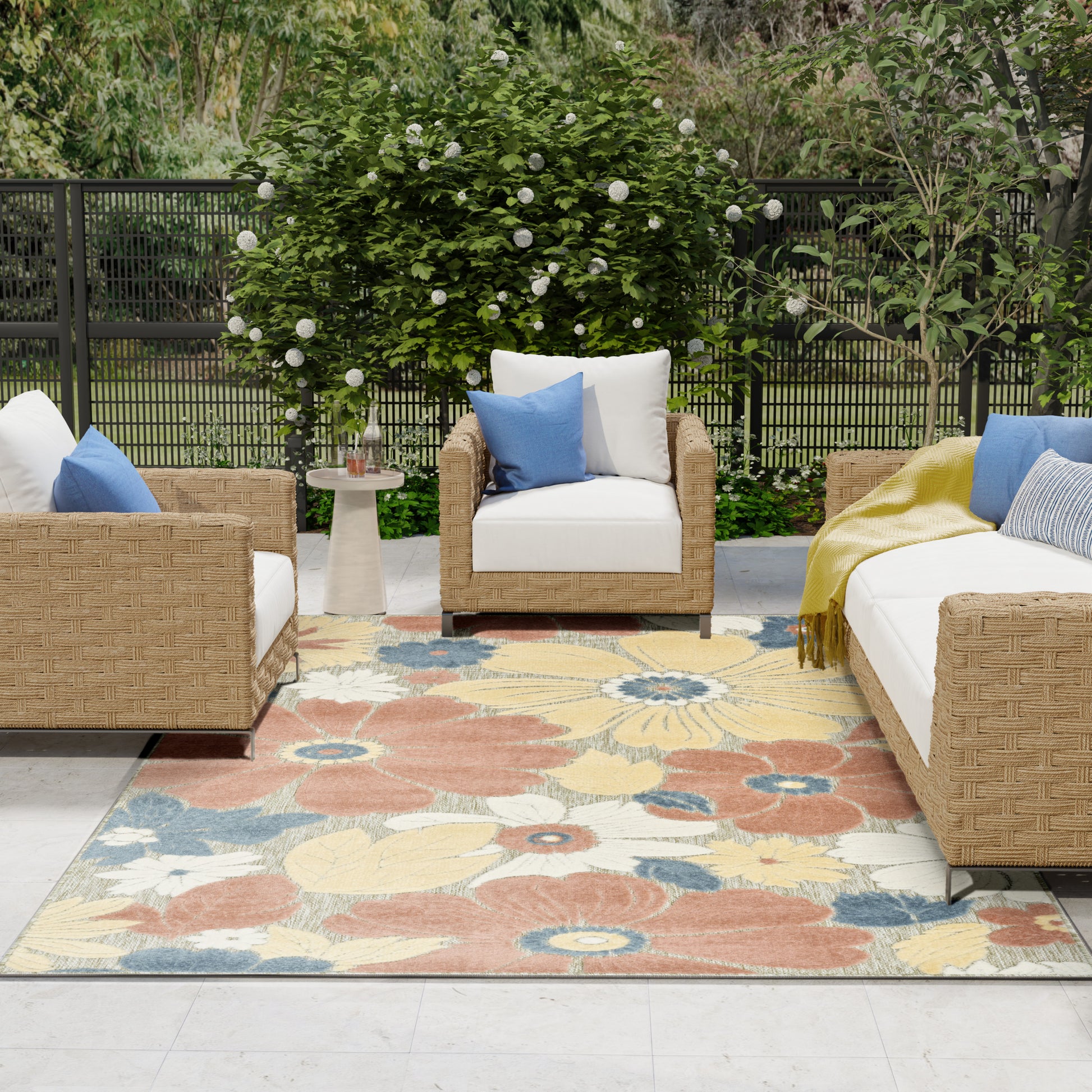 Outdoor woven rattan seating with white cushions, blue pillows, a colorful floral rug, and a round side table.