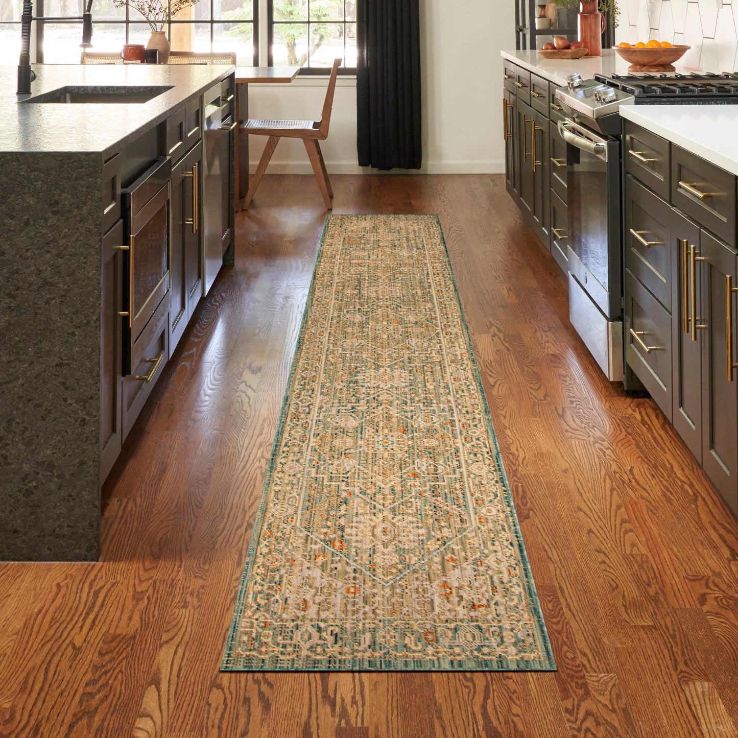 Long beige kitchen runner rug with teal border and geometric motifs on a hardwood floor between dark cabinets.