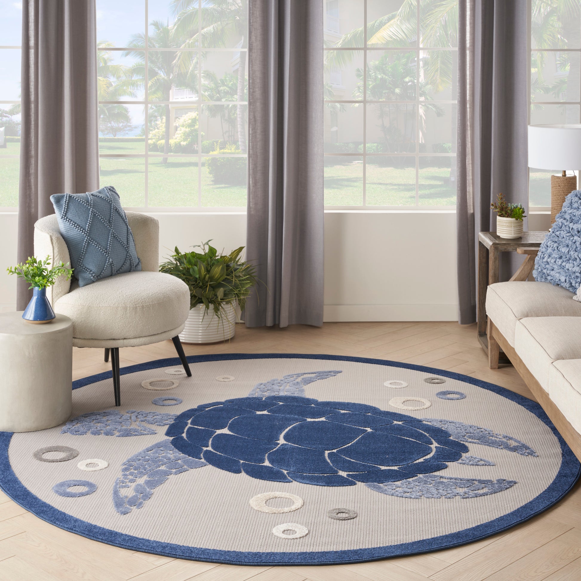 Round beige woven rug with navy turtle motif and blue border; coastal living room with blue cushions.