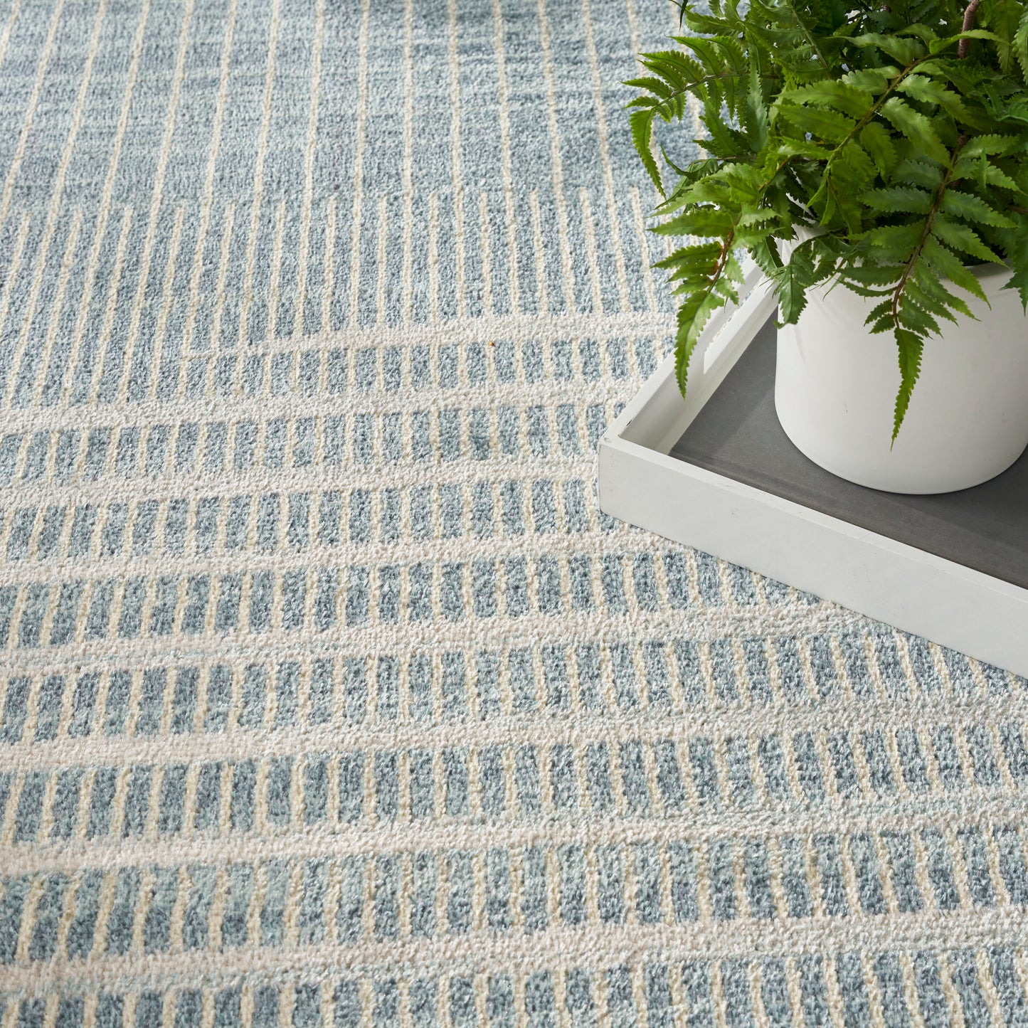Blue-gray striped woven rug with soft texture beside a white tray holding a potted fern.