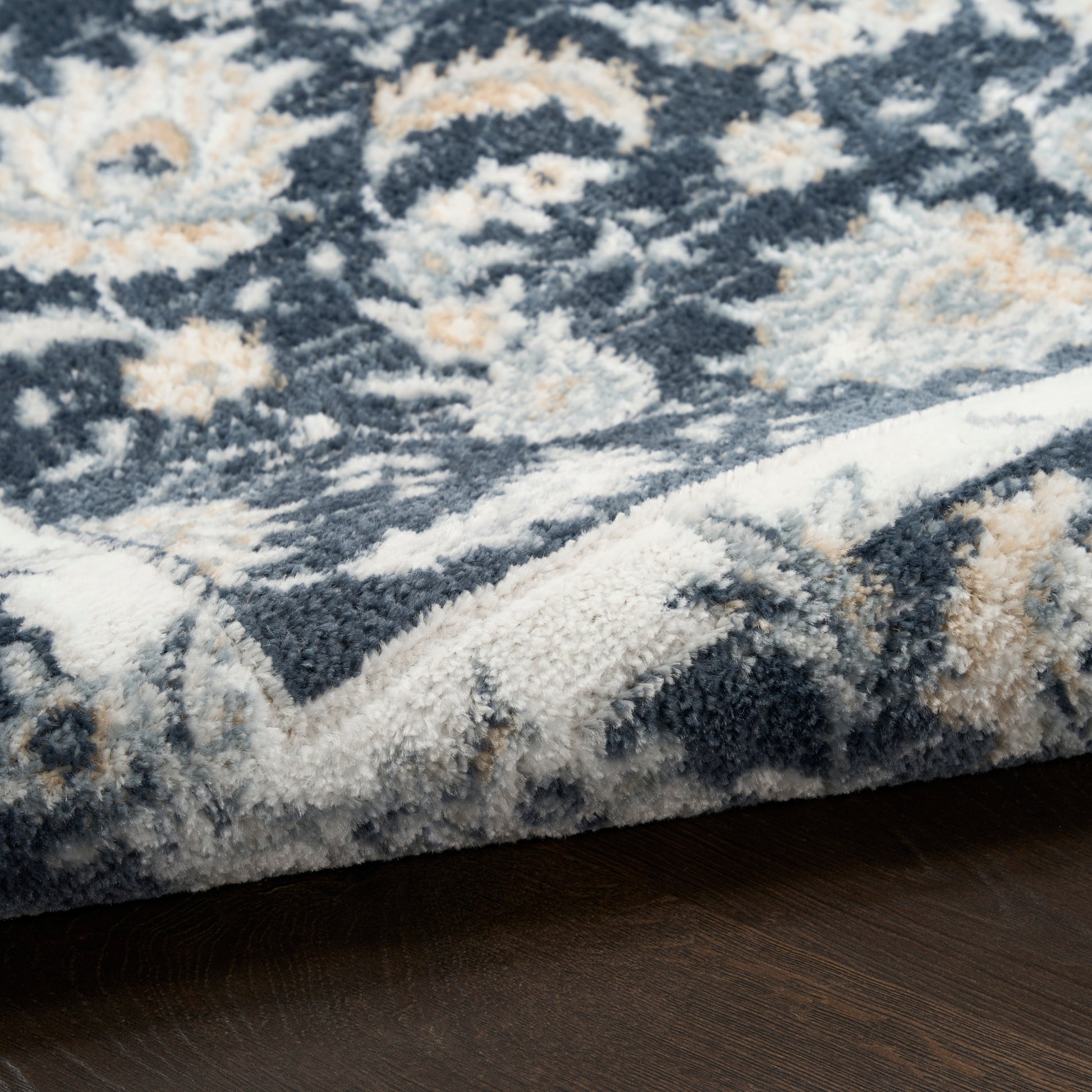 Soft textured area rug with navy blue, ivory and tan floral pattern; plush high pile and rolled edge on dark wood floor.