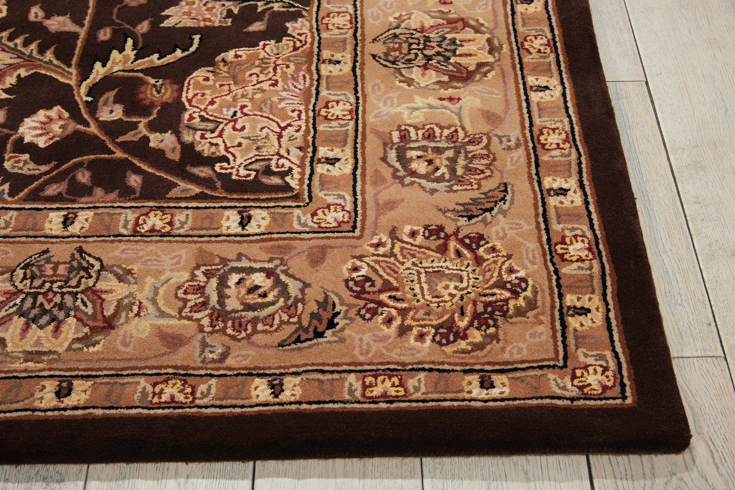 Oriental-style rug corner with brown, tan and cream floral border on light wooden floor.