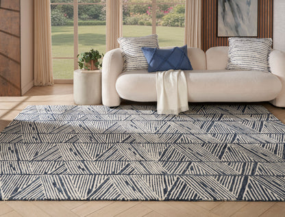 Navy and cream geometric rug on light wood floor with cream sofa, blue pillows, striped cushions.