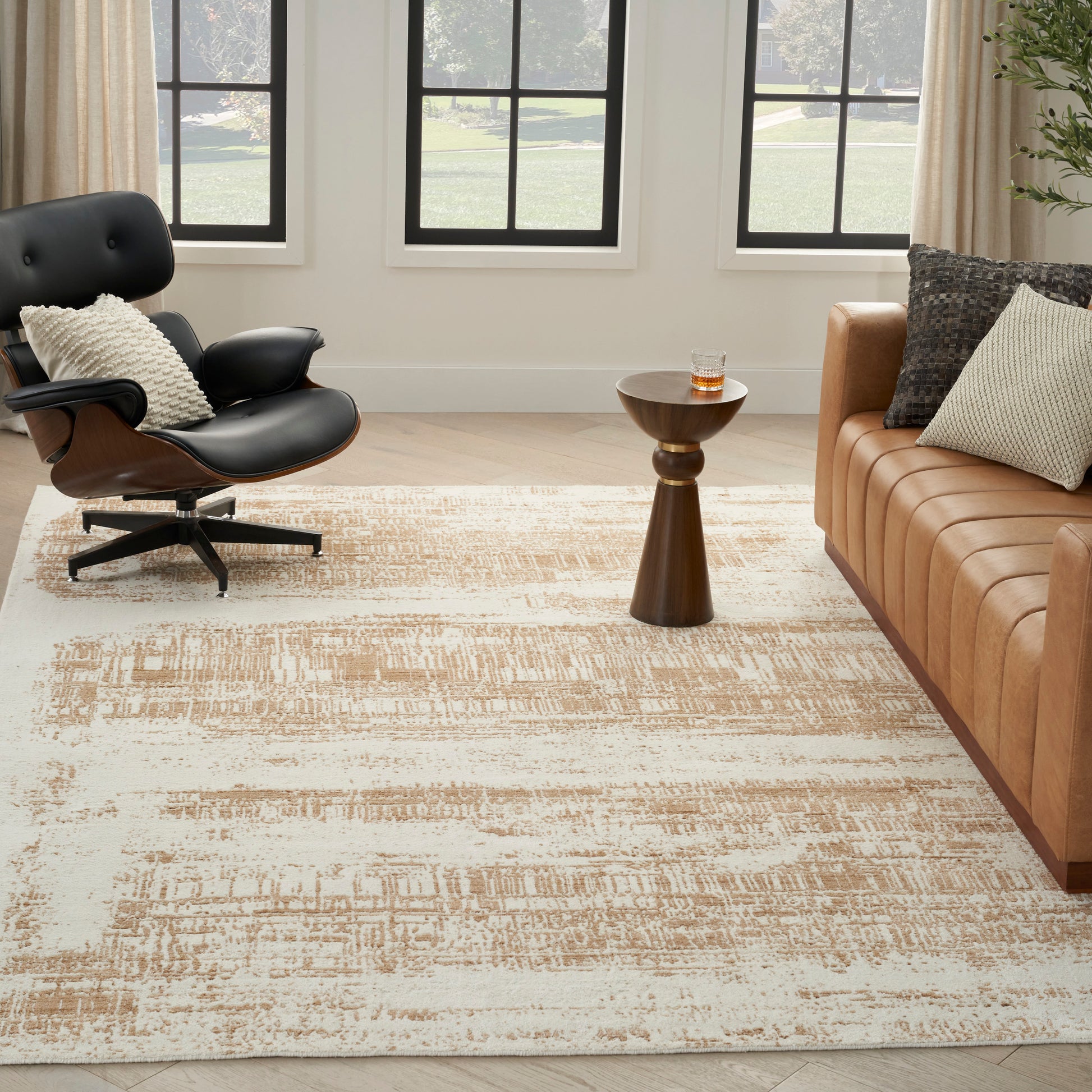 Living room with beige abstract-pattern rug, tan leather sofa, black leather lounge chair, and round wooden side table by a window.