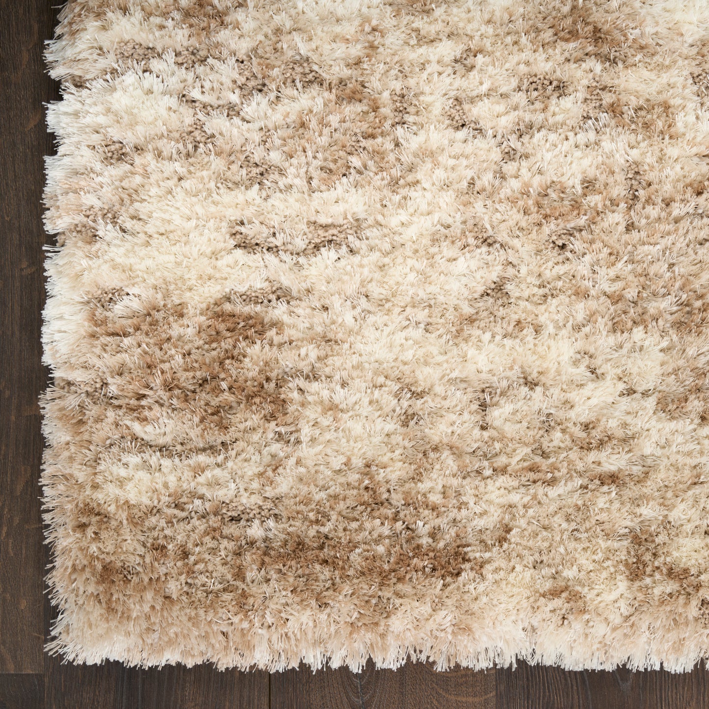 Beige shag rug with cream and tan fibers on dark hardwood floor; plush, fluffy rectangular area rug.