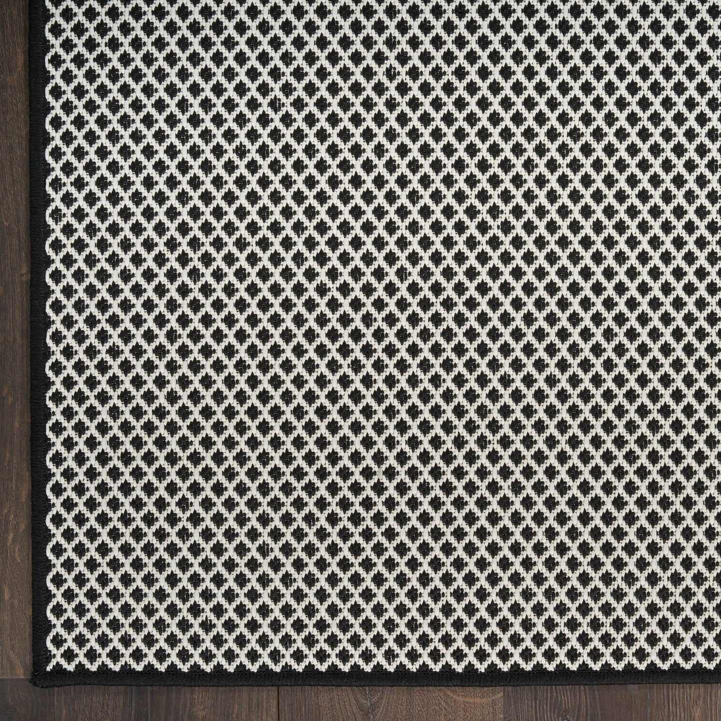 Rectangular rug with cream lattice weave on charcoal background, dark wood edge framing.