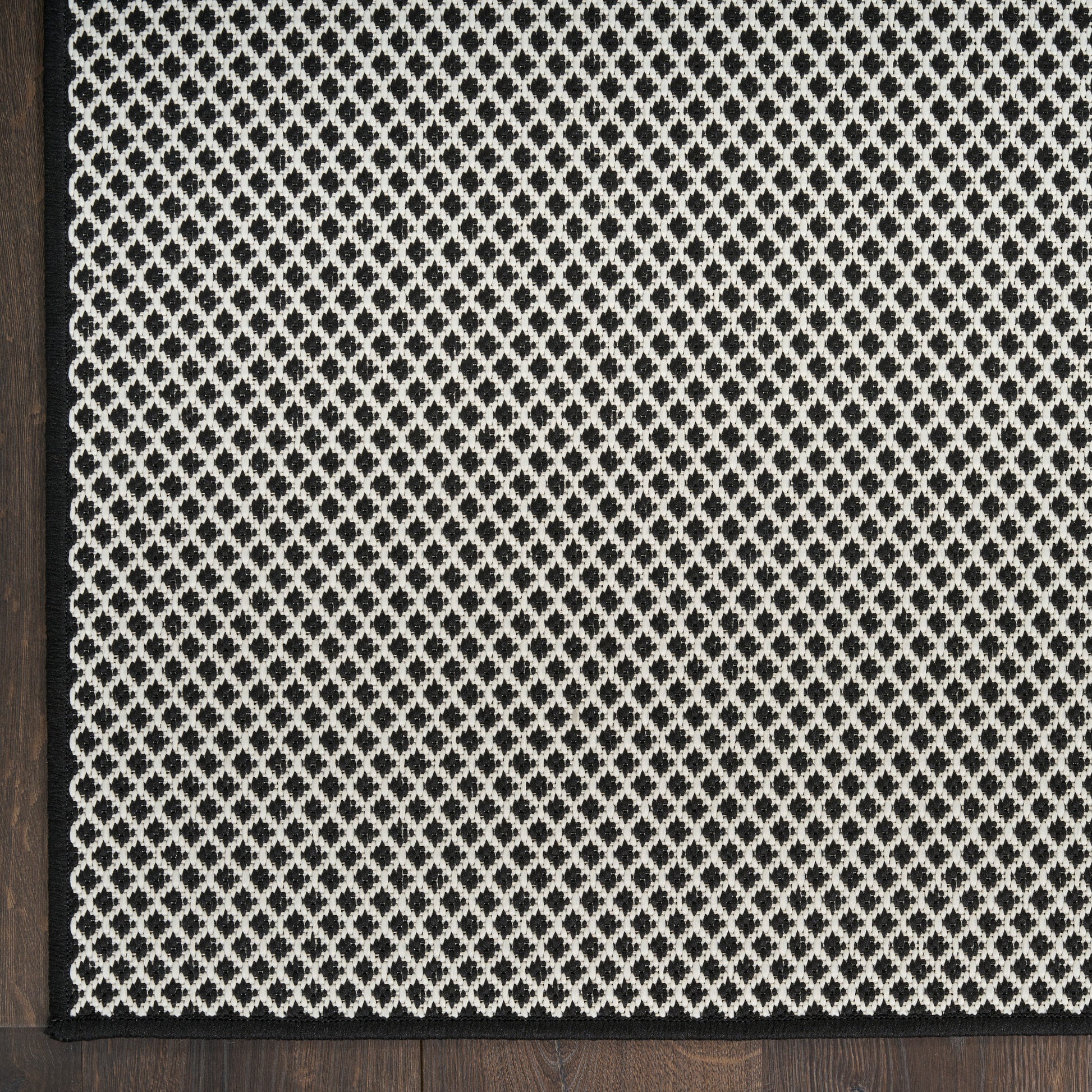 Rectangular rug with cream lattice weave on charcoal background, dark wood edge framing.