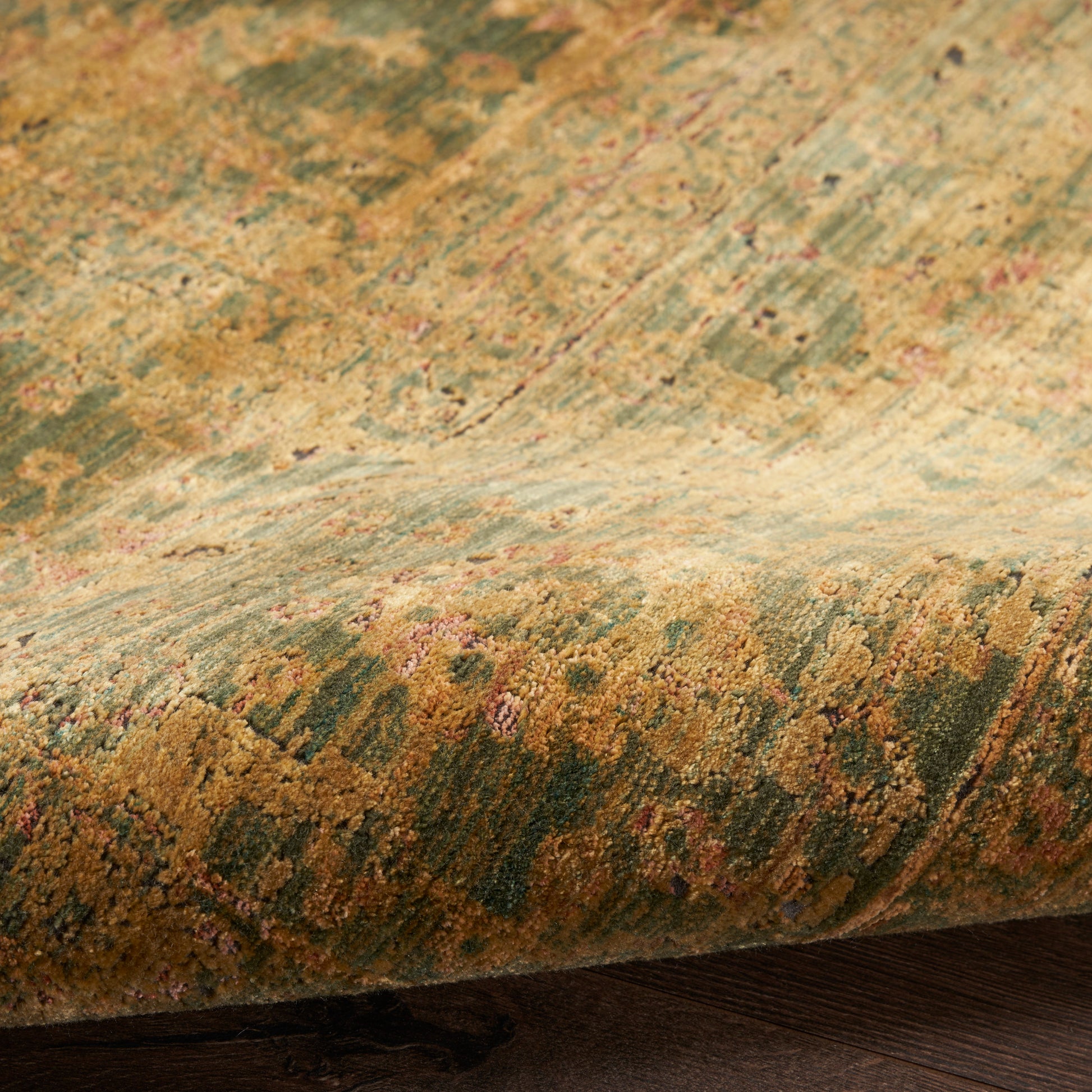Close-up of a plush oriental rug with gold, moss green and pink floral pattern resting on dark wood floor.