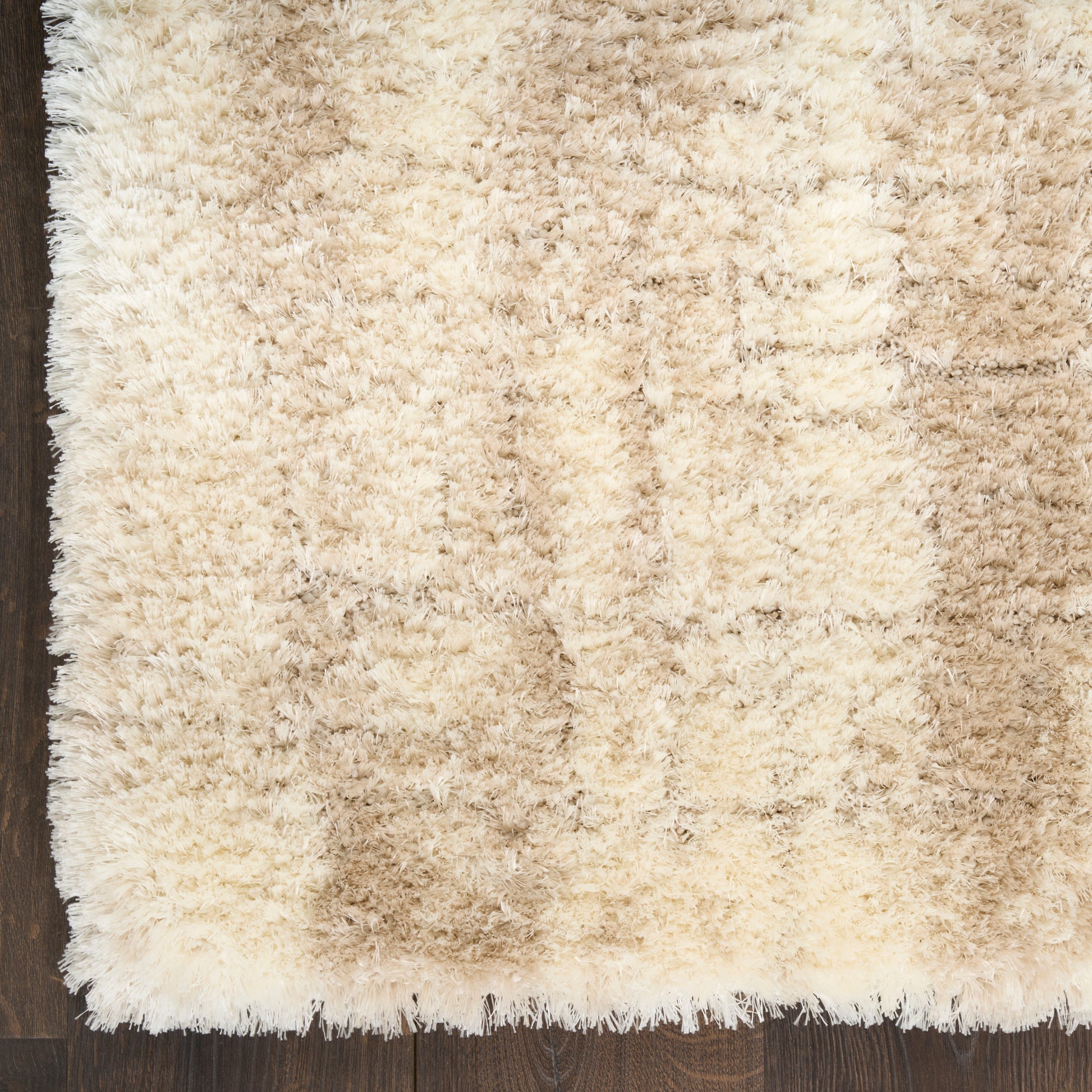 Rectangular cream shag rug with thick plush pile in beige tones and white fringe on dark wood floor.