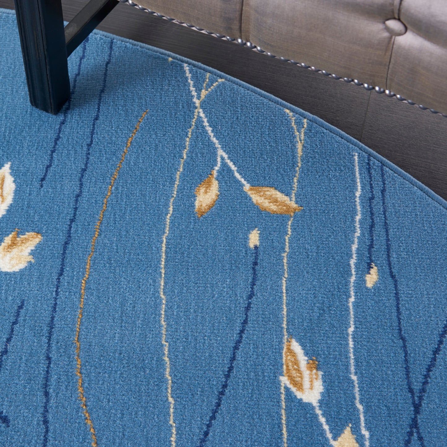 Round blue rug with tan leaf motifs and white linear patterns; woven low-pile under chair and sofa.