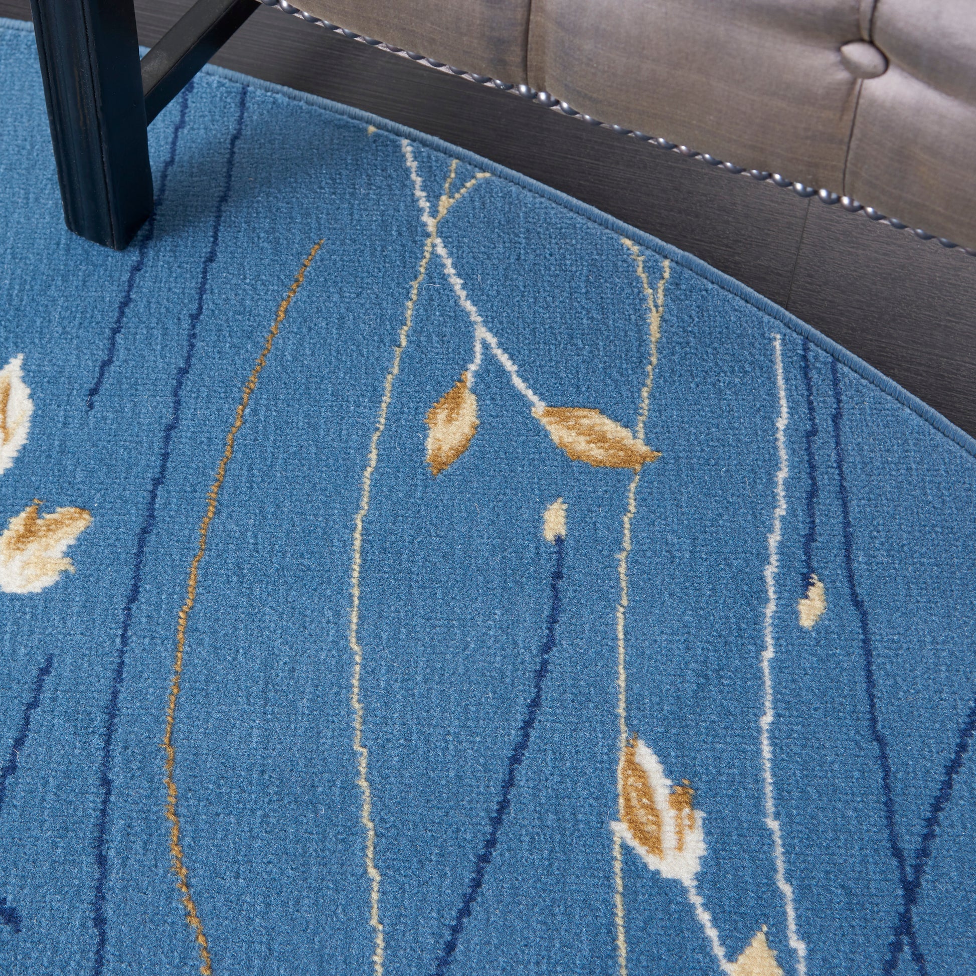 Round blue rug with tan leaf motifs and white linear patterns; woven low-pile under chair and sofa.