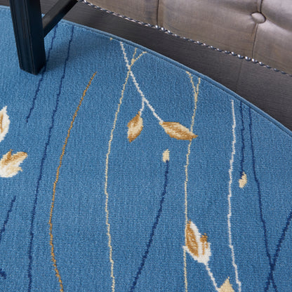 Round blue rug with tan leaf motifs and white linear patterns; woven low-pile under chair and sofa.