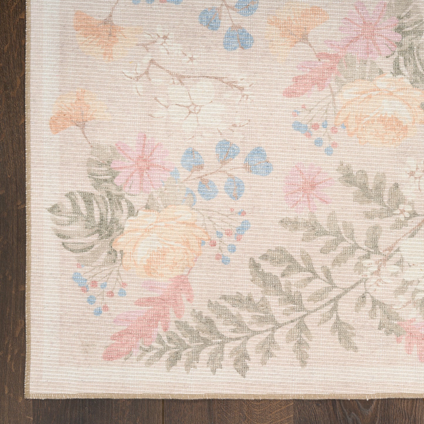 Pastel floral rug with peach roses, pink blossoms, blue accents and gray-green ferns on beige background; wood edge visible.