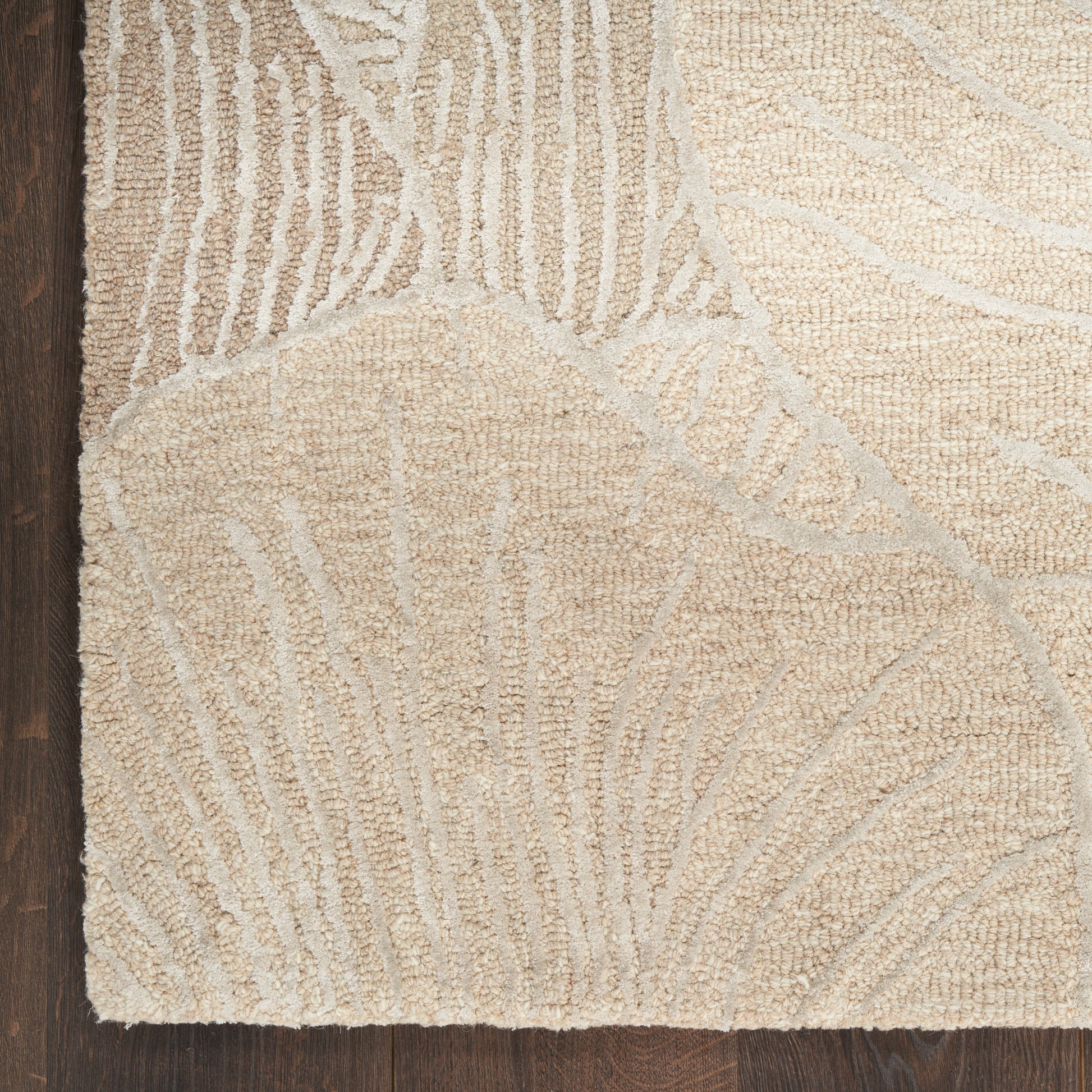 Beige textured area rug with subtle light gray abstract leaf/branch pattern on dark wood floor.